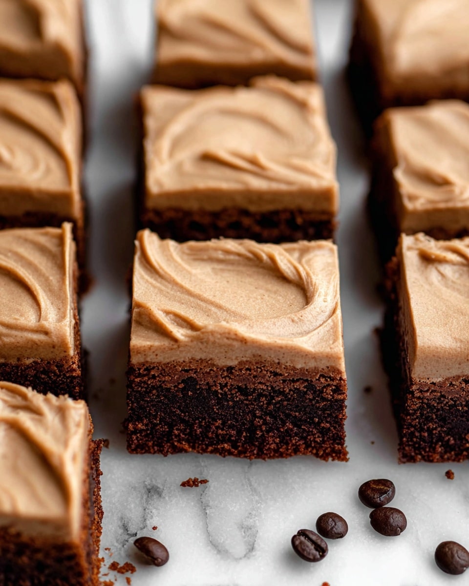 The image shows several square brownies arranged on a white marbled surface, each with two layers: the bottom layer is dark brown with a dense, moist texture, and the top layer is a smooth, light brown frosting with subtle swirl marks. The brownies are closely placed with some small crumbs visible around the edges, and a few dark brown coffee beans are scattered near the brownies. The photo focuses closely on the squares, showing the texture contrast between the rich brownie base and the creamy frosting on top. photo taken with an iphone --ar 4:5 --v 7