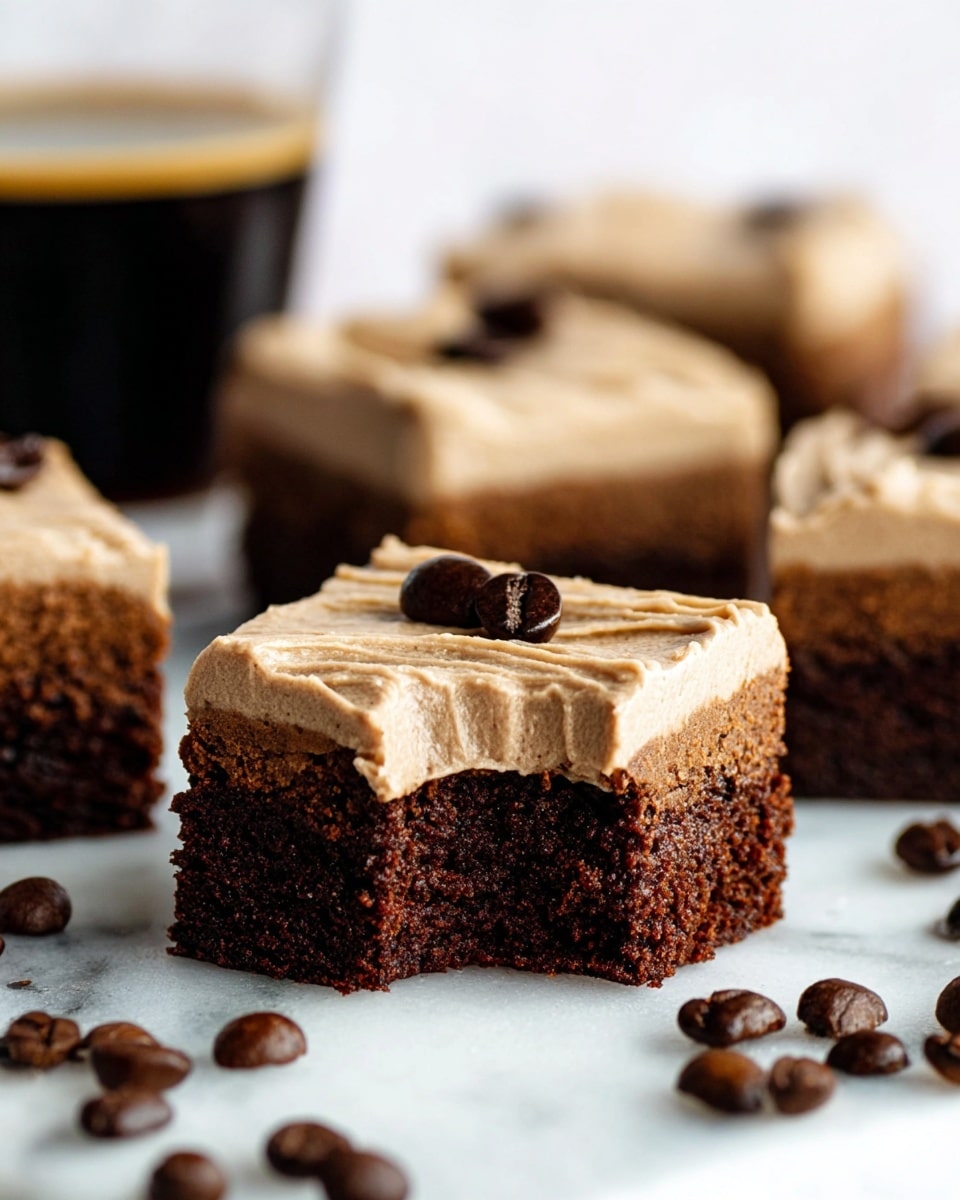 The image shows several small square brownies with two visible layers on a white marbled surface. The bottom layer is dark brown, fudgy, and moist with a soft texture, while the top layer is a thick light brown creamy frosting, smoothly spread with visible lines from spreading. On top of the frosting of the main brownie in focus, there are two small dark brown coffee beans. Around the brownies are scattered whole coffee beans, adding texture and contrast. One brownie in the front has a bite taken out, showing the dense interior clearly. The background is softly blurred with more brownies and a dark drinking glass. photo taken with an iphone --ar 4:5 --v 7