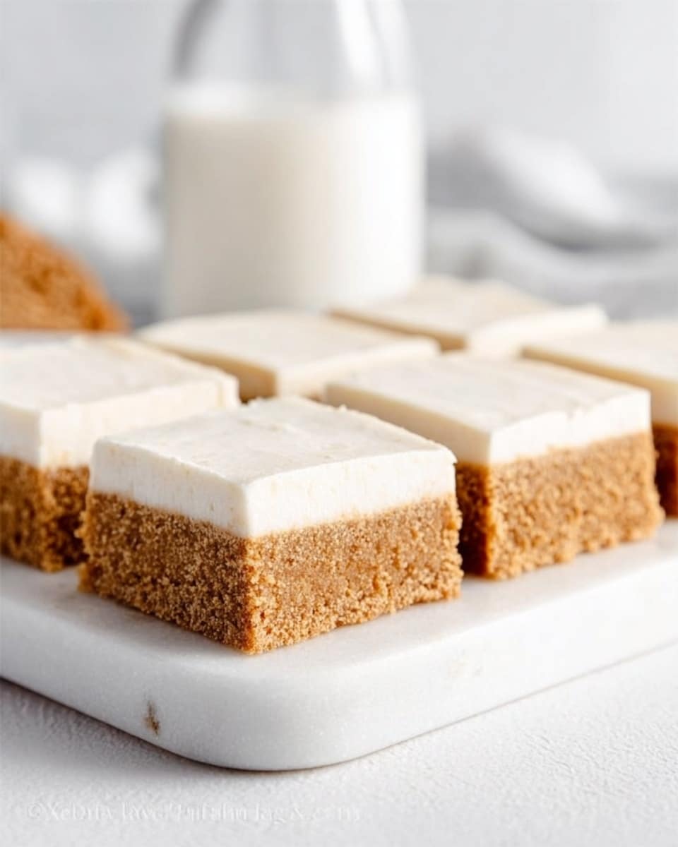 The image shows two rows of square-shaped cake bars, each with two layers. The bottom layer is a thick, spongy cake layer with a light brown color and a soft, crumbly texture. The top layer is a smooth, creamy icing that is white and evenly spread, covering the entire surface of each cake bar. The bars are placed on white parchment paper that lies on a round dark grey stone board, which is set on a white marbled surface. In the background, there is a slightly blurred glass bottle and other white-colored objects, giving a clean and bright atmosphere. Photo taken with an iphone --ar 4:5 --v 7