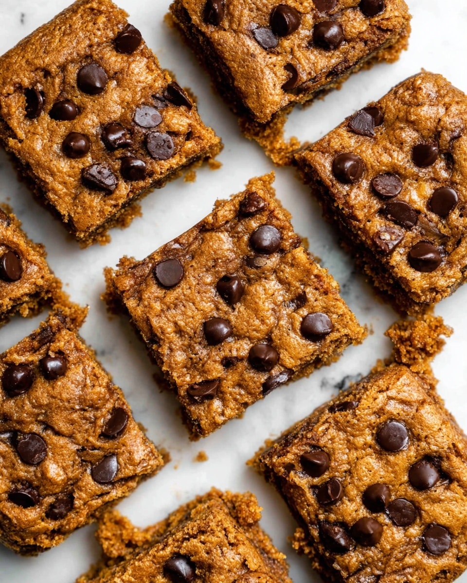 This image shows nine square chocolate chip blondies arranged closely on a white marbled surface. Each blondie is about one layer thick with a rough, crumbly brown texture and scattered shiny dark brown chocolate chips embedded on the top surface. The chips are unevenly spaced and slightly melted around the edges, blending into the blondie's moist-looking top layer. The blondies have clean sharp edges and some small crumbs visible on the surface beneath them. Photo taken with an iphone --ar 4:5 --v 7
