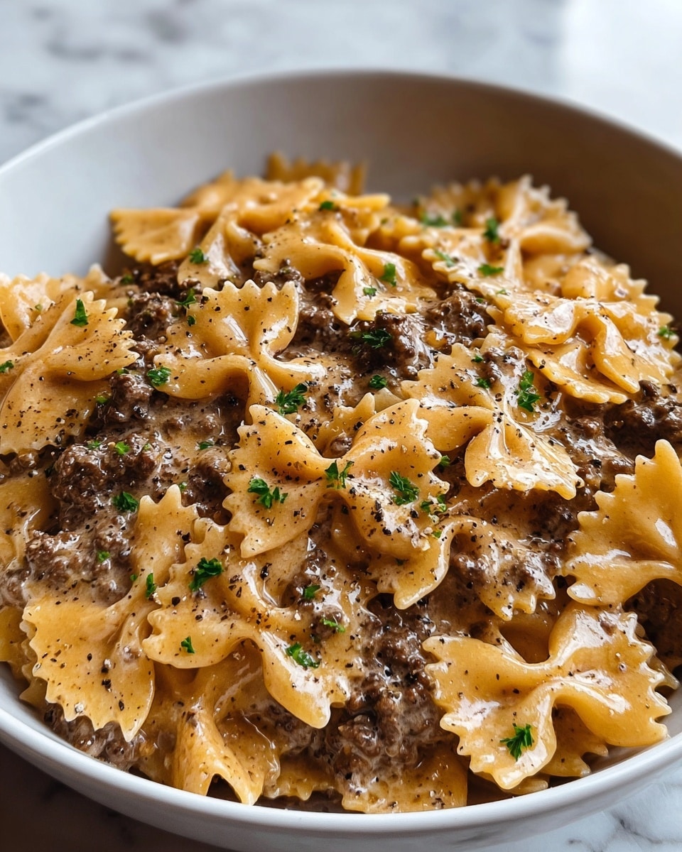 A white bowl filled with farfalle pasta coated in a creamy light beige sauce mixed evenly with ground beef pieces that are dark brown, creating a textured contrast. The pasta layer is thick and spread across the bowl with a slight shine from the sauce. Small green parsley bits are sprinkled over the dish, adding a fresh color pop. Black pepper flakes are scattered visibly on top, enhancing the rich and savory look. The bowl sits on a white marbled texture surface. photo taken with an iphone --ar 4:5 --v 7