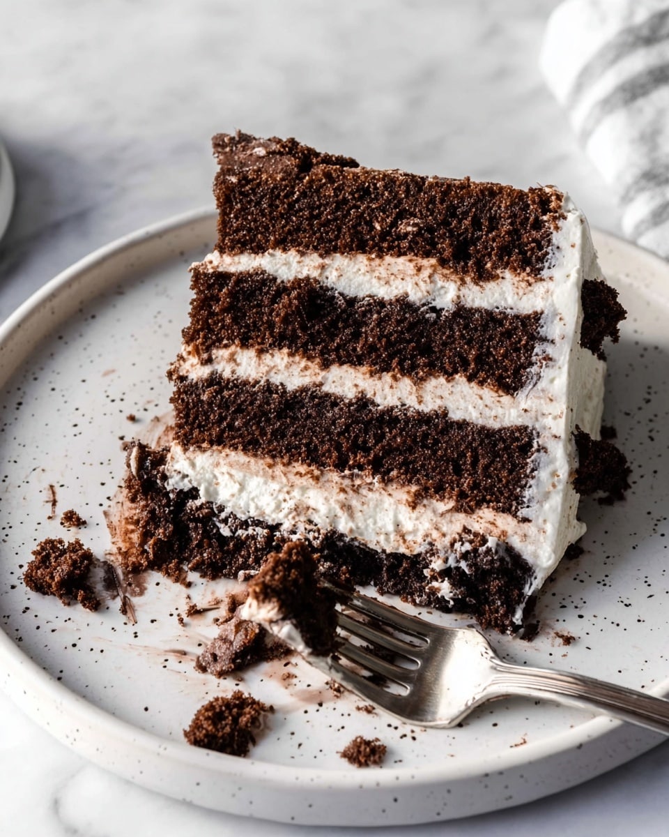 A slice of chocolate layer cake is shown resting on a white plate with small gray speckles, placed on a white marbled surface. The cake has three thick layers of dark brown chocolate sponge, each separated by two layers of white cream frosting that looks light and fluffy. There is some frosting and chocolate crumb smeared on the plate near a silver fork lying next to the cake slice. A few small chocolate crumbs are scattered on the white marbled surface below. The overall look is soft and moist with a contrast between the dark chocolate and white cream. photo taken with an iphone --ar 4:5 --v 7