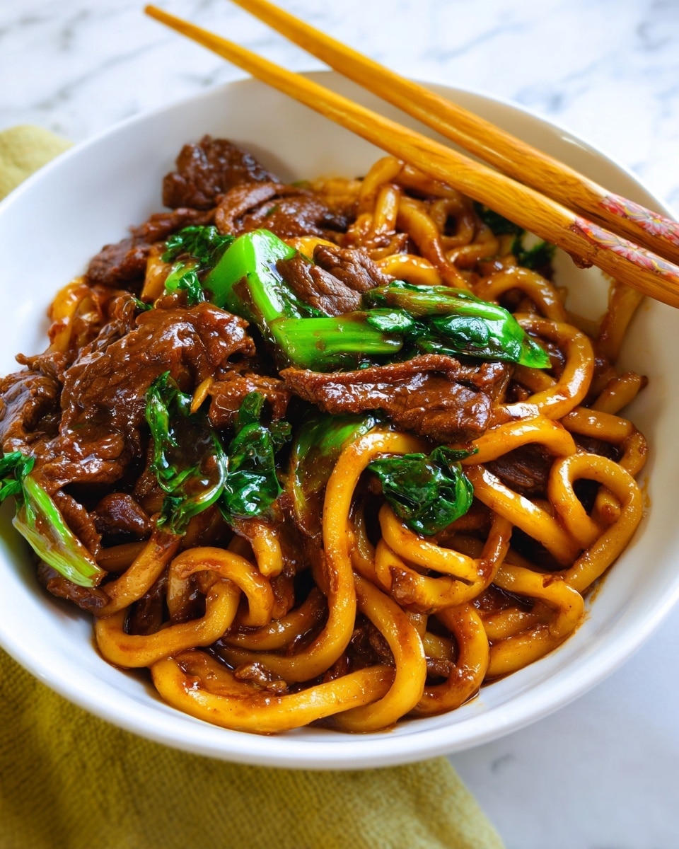 A close-up of a white bowl filled with thick, golden-brown noodles coated in a glossy dark sauce, mixed with tender slices of rich brown beef and bright green leafy vegetables scattered throughout; the noodles twist around each other, creating a textured, dense layer on top, while the beef pieces are nestled between and beneath the noodles, adding depth and color contrast; in the background, a pair of light wooden chopsticks rest on the edge of the bowl, all placed on a white marbled surface. photo taken with an iphone --ar 4:5 --v 7