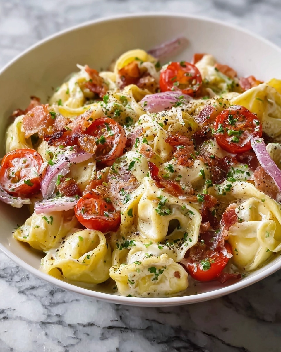 A white bowl filled with creamy tortellini pasta layered with soft yellow cheese-filled pasta pieces, halved bright red cherry tomatoes, small crispy chunks of browned bacon, and thin slices of light purple onion mixed throughout. The dish is sprinkled with finely chopped green herbs and a dusting of black pepper, all resting on a white marbled textured surface. The creamy sauce lightly coats the pasta, giving it a smooth and rich look. photo taken with an iphone --ar 4:5 --v 7