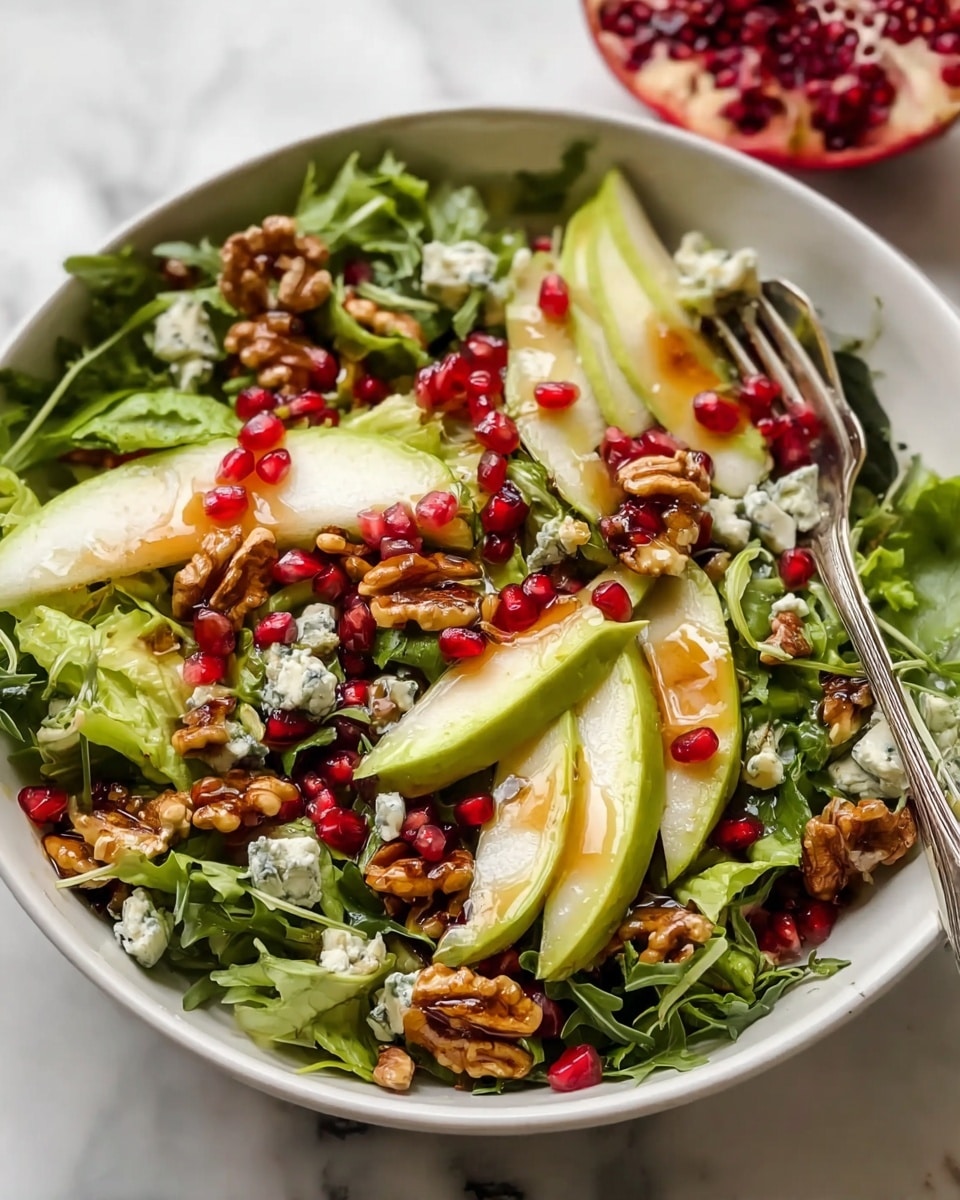 A fresh salad is served in a white bowl placed on a white marbled surface, featuring a mix of green leafy lettuce as the base layer, topped with thin slices of light green avocado and pale pear slices arranged evenly. Bright red pomegranate seeds are scattered throughout, adding pops of color, while small chunks of creamy blue cheese and golden brown walnuts are spread across the top. The salad is lightly drizzled with a glossy dressing that gives a slight shine on the walnuts, making the whole dish look fresh and vibrant. A silver fork rests in the bowl, ready for serving. Photo taken with an iphone --ar 4:5 --v 7