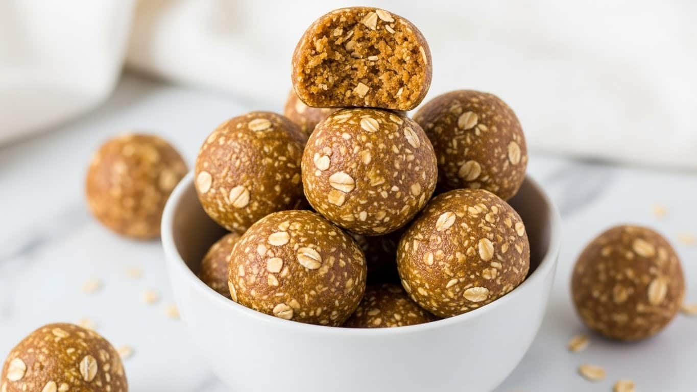 A white bowl filled with round, light brown energy balls that have visible oats mixed inside, giving them a rough texture. There are eight energy balls stacked in the bowl, with one on top partially broken to show a crumbly inside with tiny oat pieces. Around the bowl, a few energy balls rest on a white marbled surface, and a soft white cloth is draped in the background. The light is soft, highlighting the natural texture of the oats and the smoothness of the balls. photo taken with an iphone --ar 4:5 --v 7
